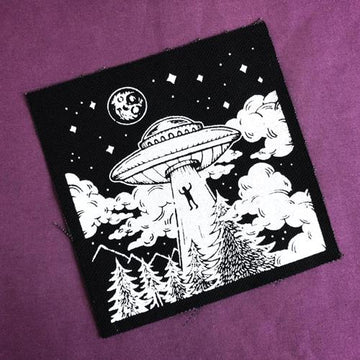 Screen printed image of person being pulled into a flying saucer at night amongst trees and mountains. White ink on black canvas sew on patch. Art by Print Ritual.