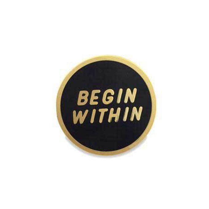 Black circle enamel pin with "begin within" in gold with gold border.
